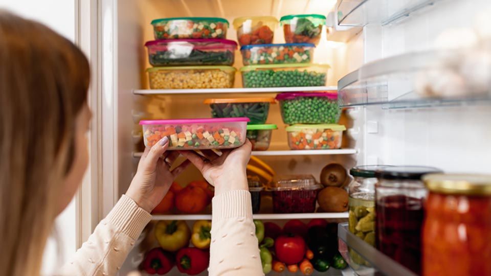 Close up shot of woman taking a plastic container with mixed vegetables from refrigerator
